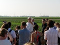 A group of people standing in a field, wind turbines are far in the background